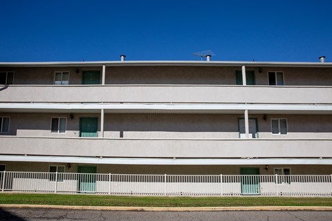 the side of a white building with green doors and a white fence