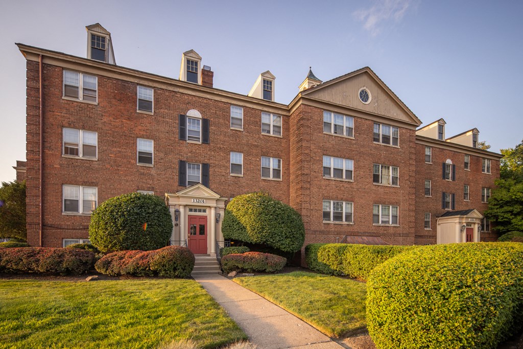 a red brick building with a sidewalk and bushes in front of it