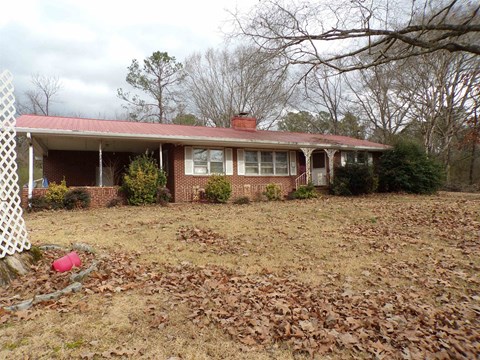 A house with a red roof and white trim is surrounded by trees and a white fence.