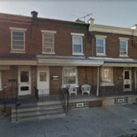 the front of a red brick house with tables and chairs on the porch