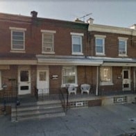 the front of a red brick house with tables and chairs on the porch