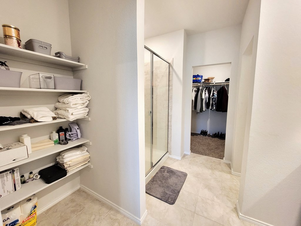 a walk in closet with shelves and a glass shower