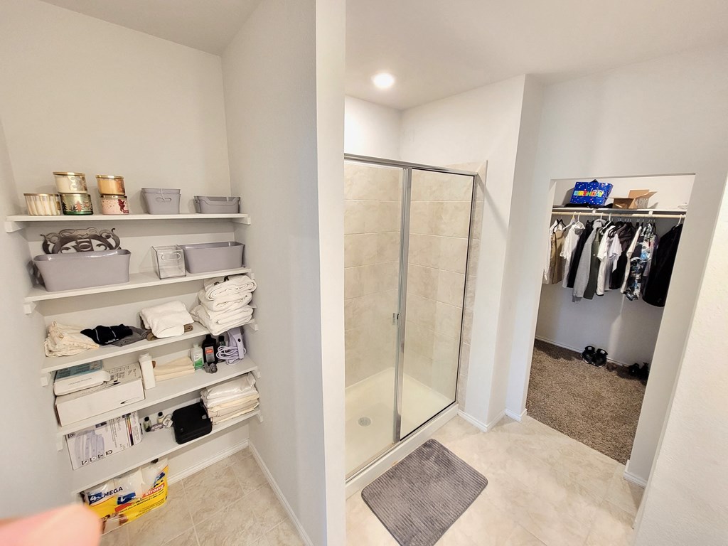 a walk in shower and shelves in a closet in a bathroom