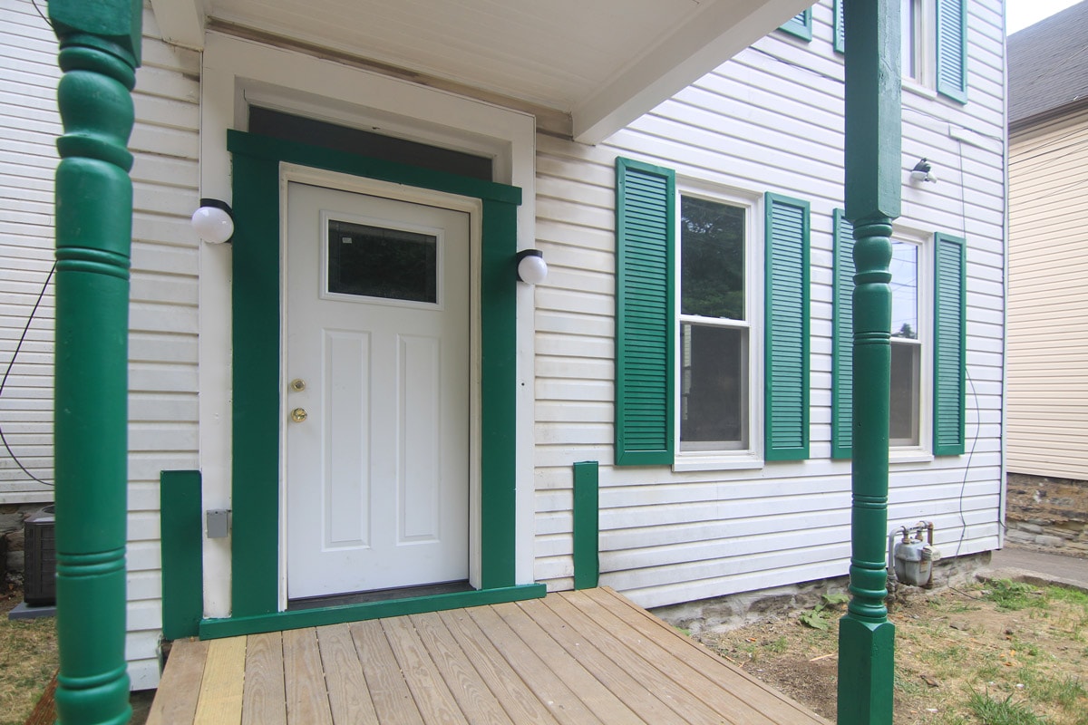 A white door with green trim is on the front porch of a house.