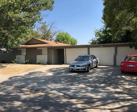 A silver car is parked in front of a house with a red car parked in the driveway.