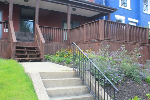 A wooden deck with a metal railing and steps leading up to a house.