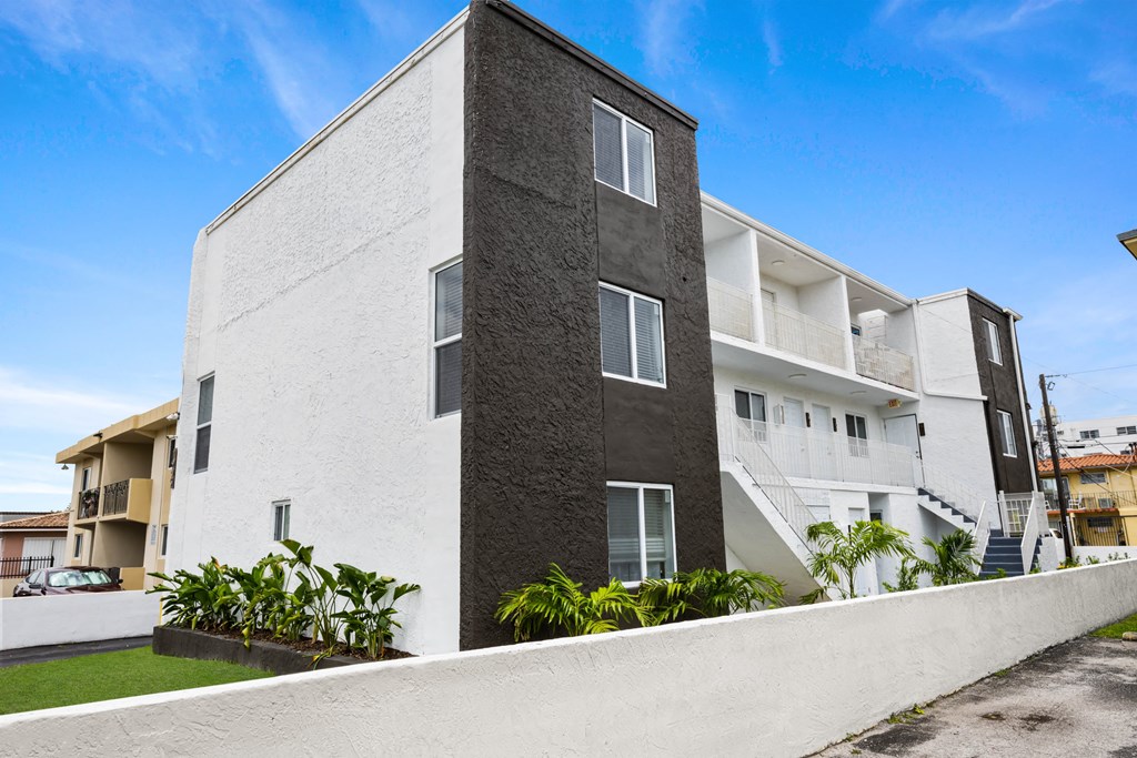 A modern two-story building with a white and grey exterior and a landscaped front yard.