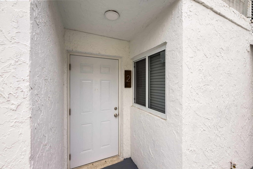 A white door with a window to the right is in a white building.