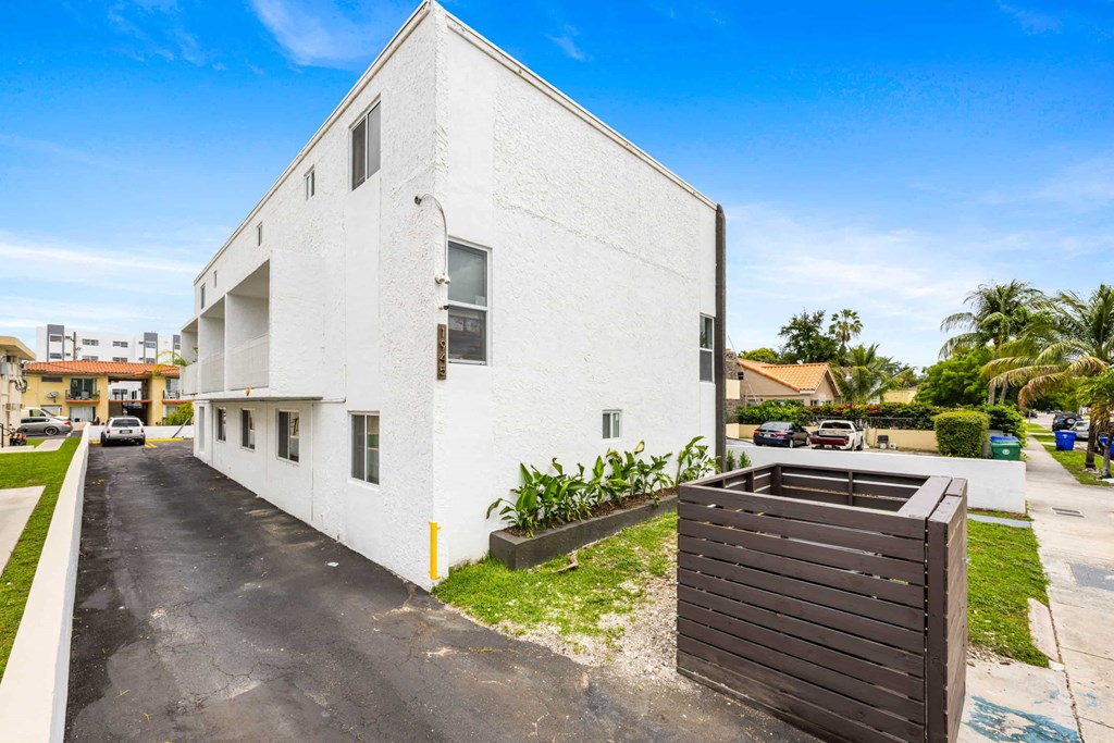 A white building with a brown dumpster in front of it.