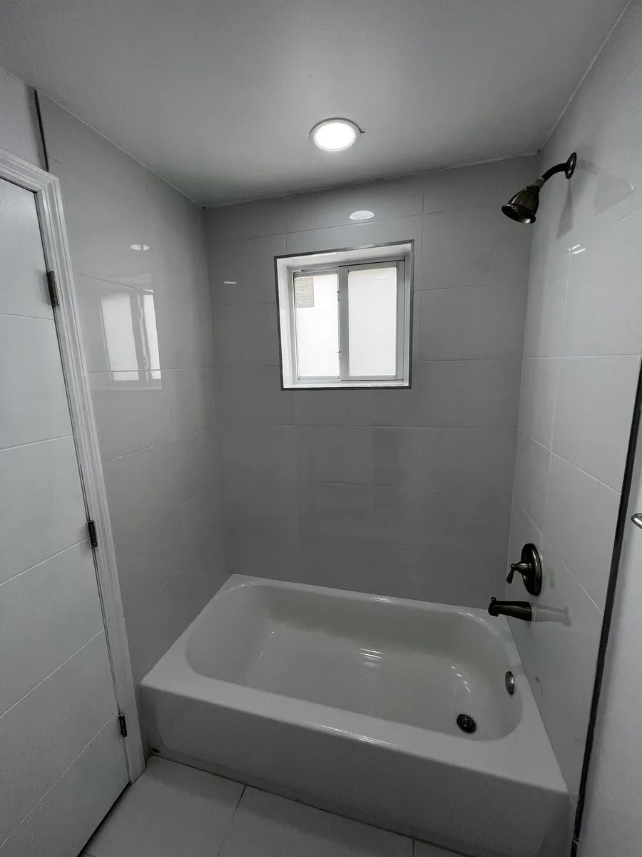 A white bathroom with a tub and a window.