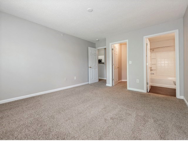 a spacious living room with carpeting and a door to a bathroom