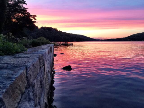 a stone wall next to a lake at sunset