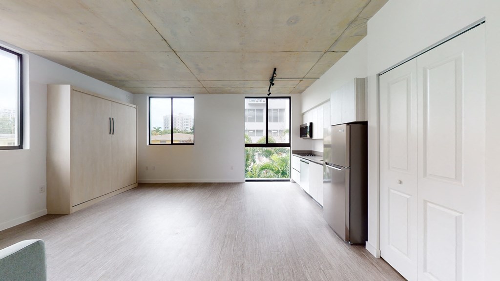 an empty living room with a kitchen and a large window