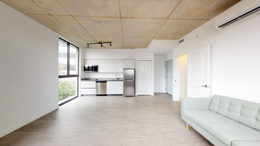 an empty living room with a white couch and a kitchen