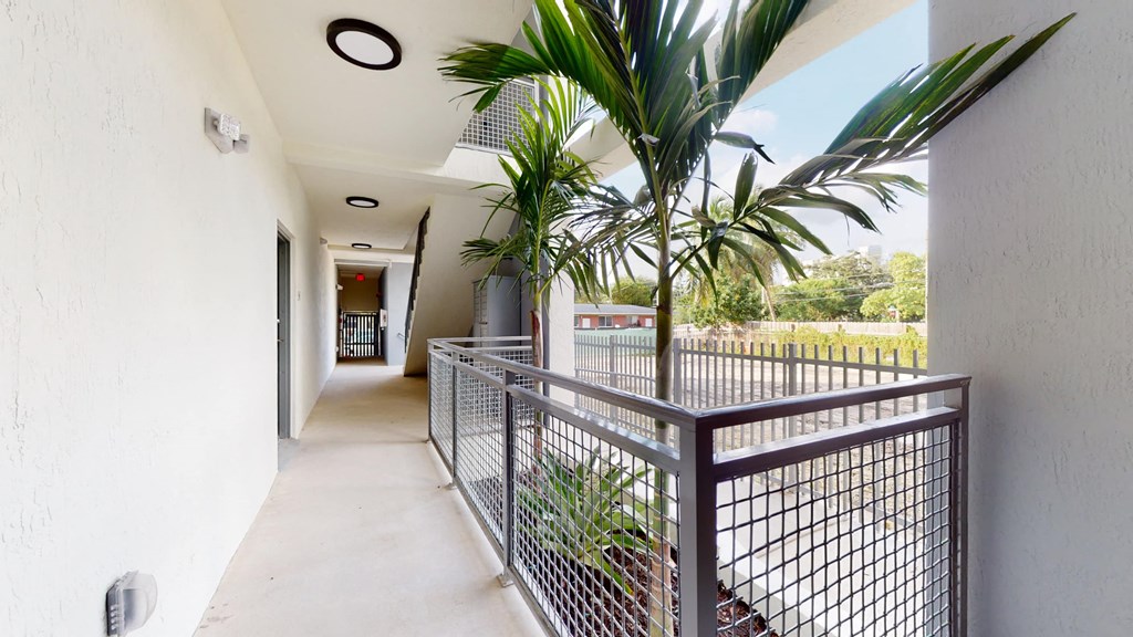 a long hallway with a metal railing and a palm tree