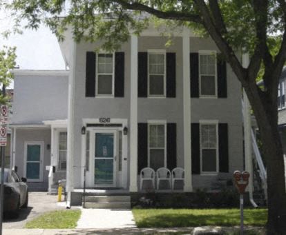 a white house with black shutters and a tree in front of it