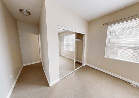 A room with a carpeted floor and a window with blinds.