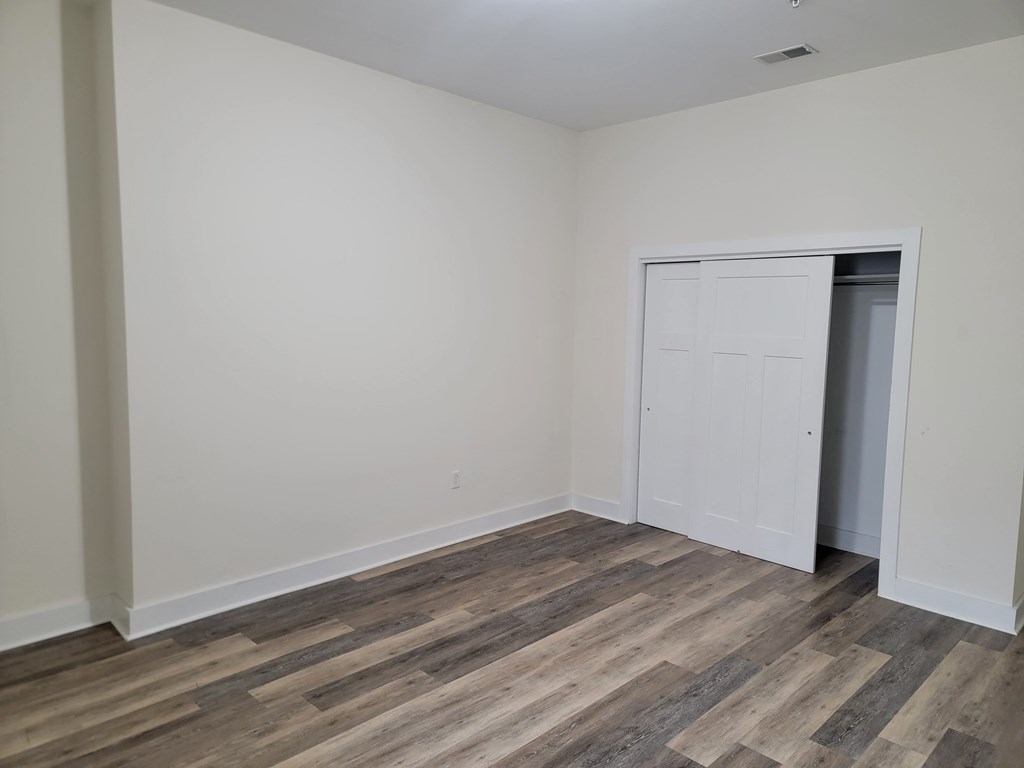 a bedroom with white walls and wood flooring and a closet