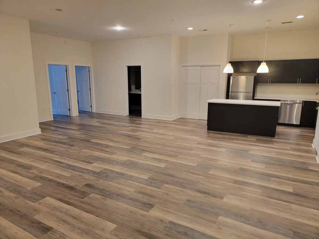 an empty living room with wooden floors and a kitchen