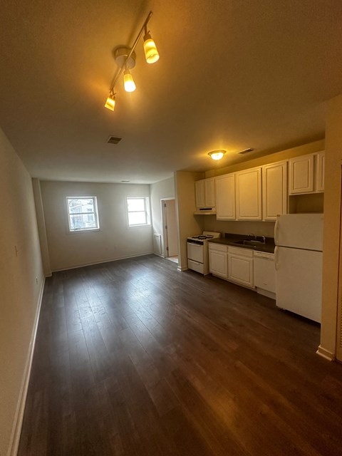 an empty living room and kitchen with wood floors and white cabinets