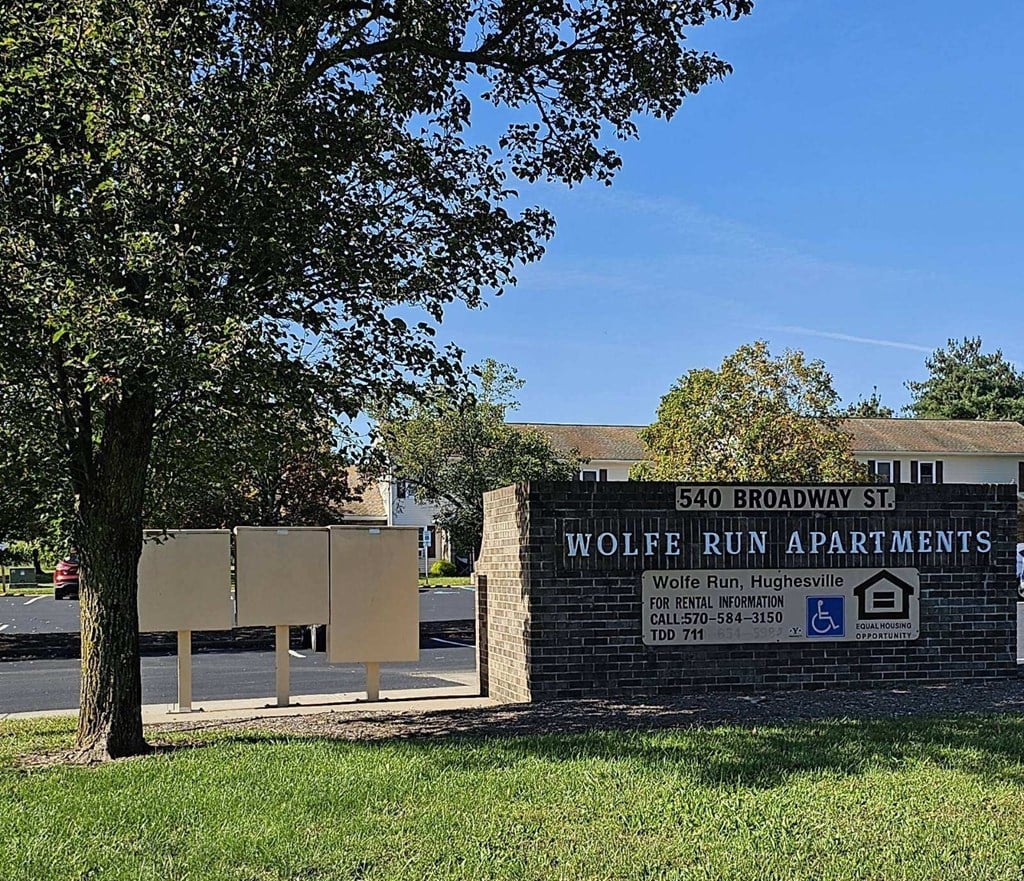 a sign for the wolfe run apartments in front of a tree