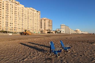 two blue chairs on the beach with a bulldozer in the background