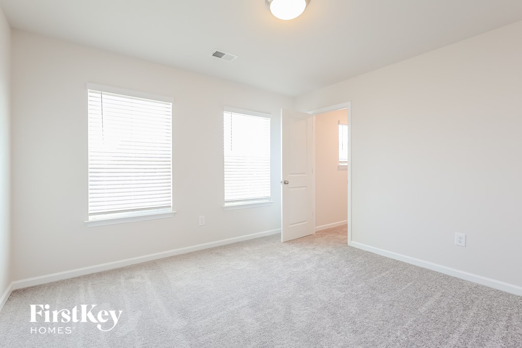 A spacious room with a carpeted floor and two windows with blinds.