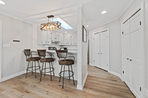 A kitchen with white cabinets and a bar area with three stools.