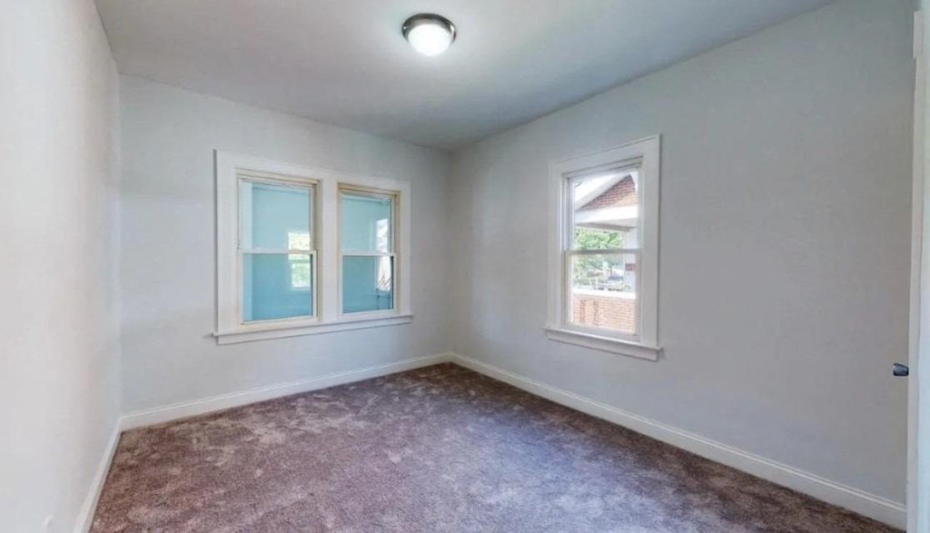 an empty room with two windows and a carpet
