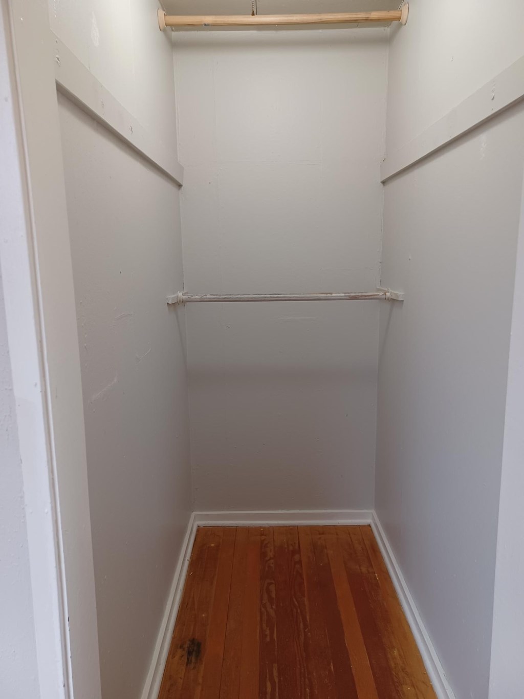 A small white closet with a wooden shelf and a wooden floor.