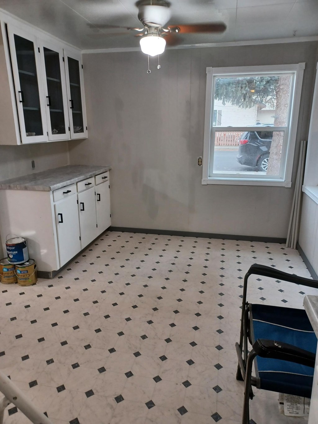 A kitchen with white cabinets and a window with a view of a street.