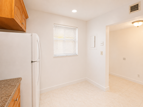 A kitchen with a white refrigerator and a window with blinds.