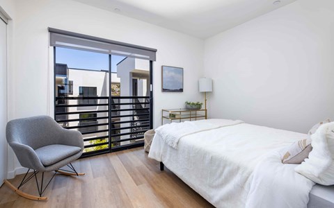 A bedroom with a large bed, a chair, and a window with blinds.