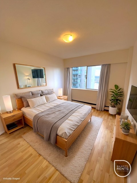 A bedroom with a large bed, a nightstand with a lamp, and a window with curtains.