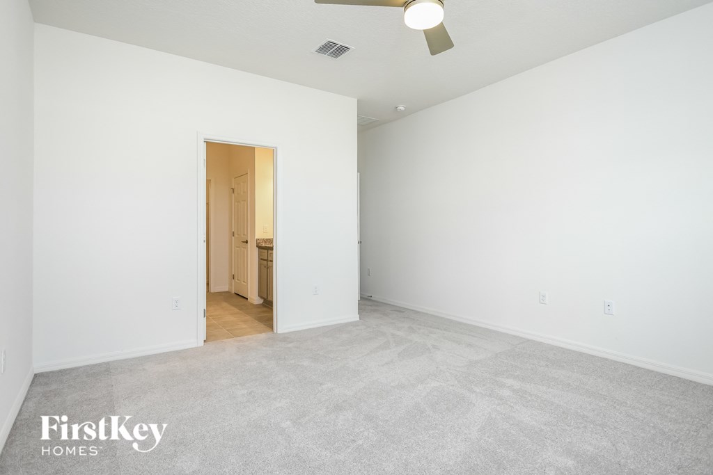 A spacious empty room with a carpeted floor and a ceiling fan.