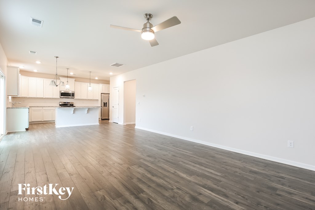 an empty living room with a ceiling fan and a kitchen