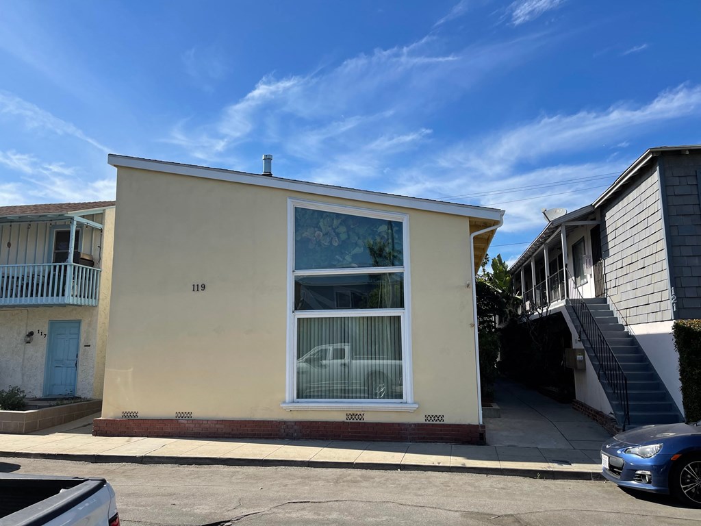 A blue car is parked in front of a yellow house.