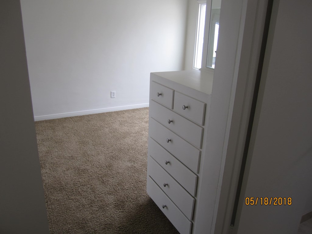 A white dresser with a mirror on top is in a room with a carpeted floor.