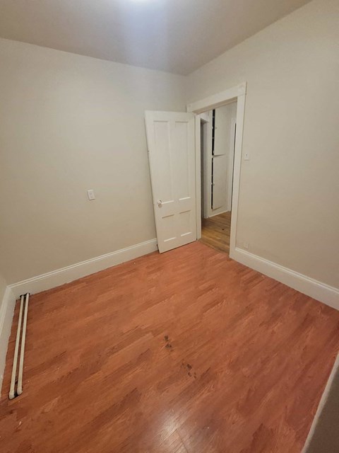 a bedroom with wood flooring and a door to a hallway