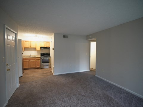 A room with a carpeted floor and a doorway leading to a kitchen.