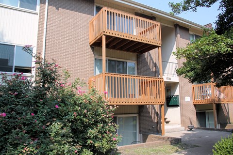 Apartment building with a balcony and bushes in front.