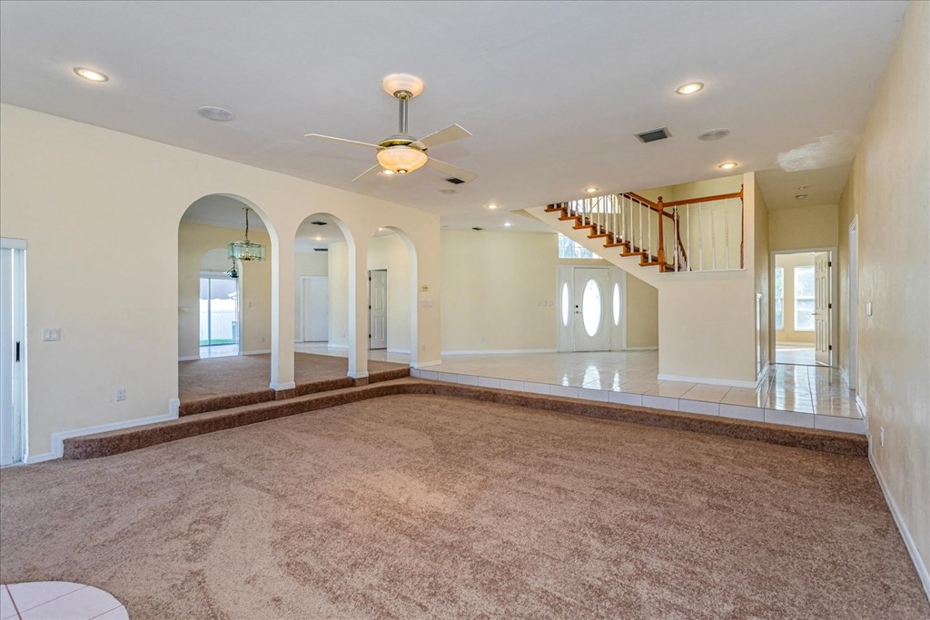 A spacious living room with a carpeted floor and a staircase in the background.