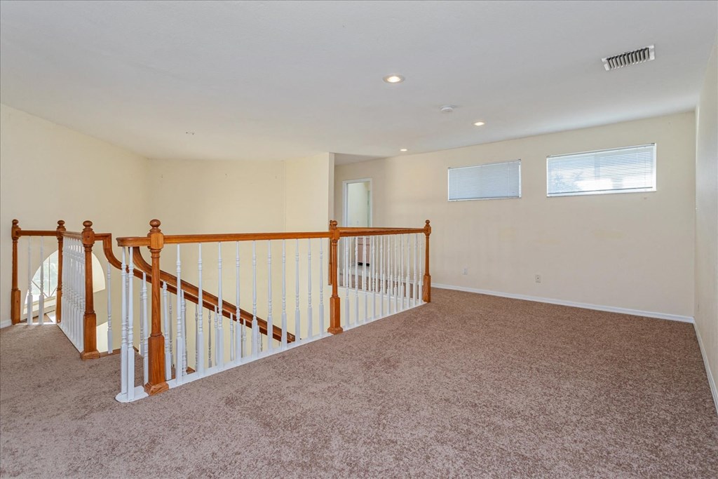 A room with a carpeted floor and a staircase with white railings.