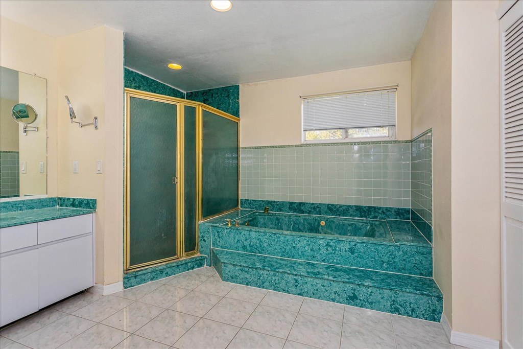 A bathroom with a green tiled shower and a white vanity.