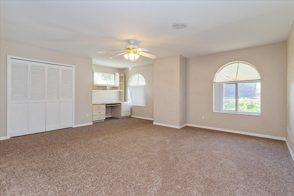 A spacious room with a carpeted floor and a ceiling fan.
