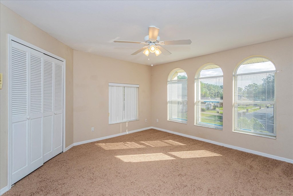 A room with a ceiling fan and three windows.