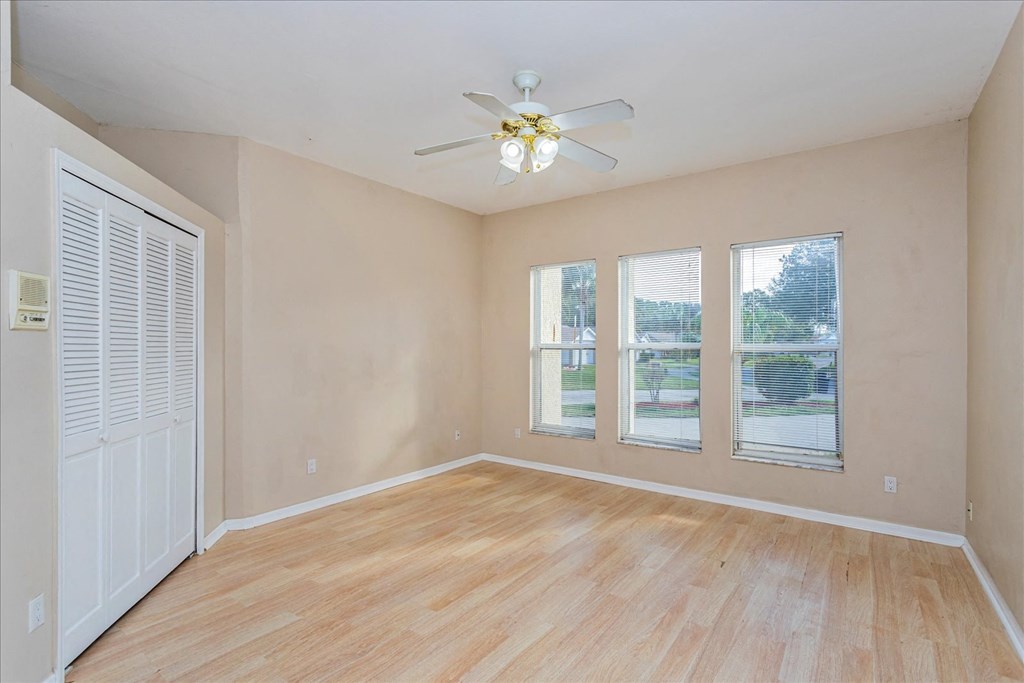 A room with a ceiling fan and three windows.