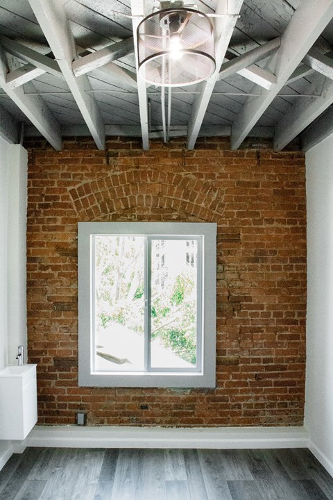 A room with a brick wall and a window showing trees outside.