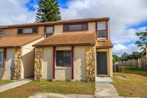 A two-story house with a brown roof and stone pillars.