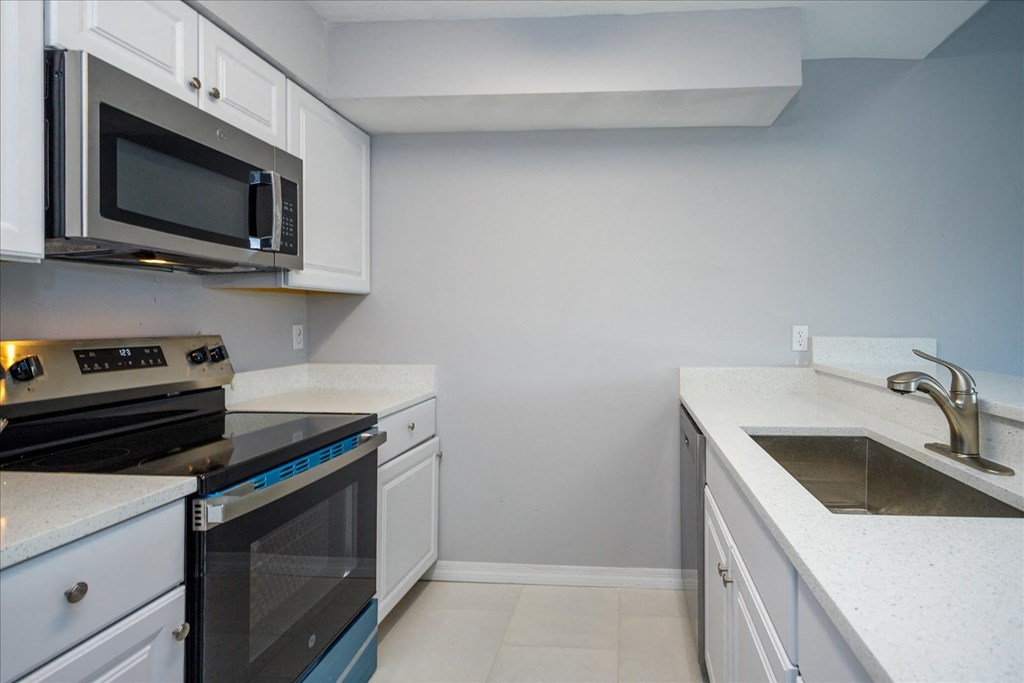 A kitchen with white cabinets and a black microwave above the stove.